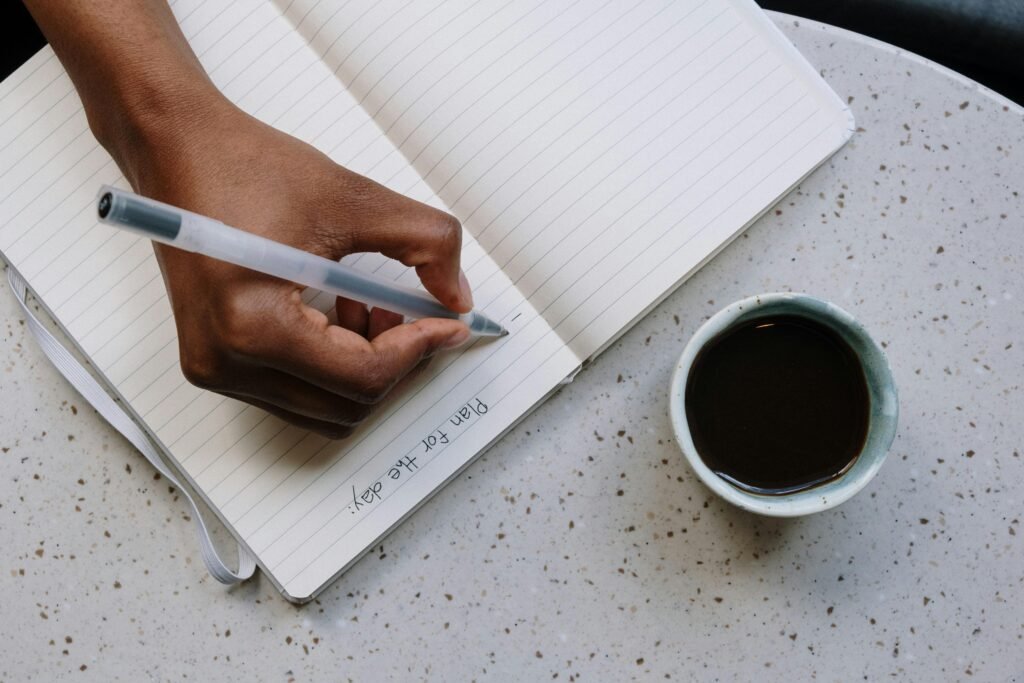 Close-up of a hand writing in a planner next to a cup of coffee.
