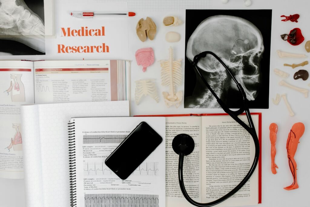 Flat lay of medical research materials with anatomy models, open books, X-ray, stethoscope, and smartphone.