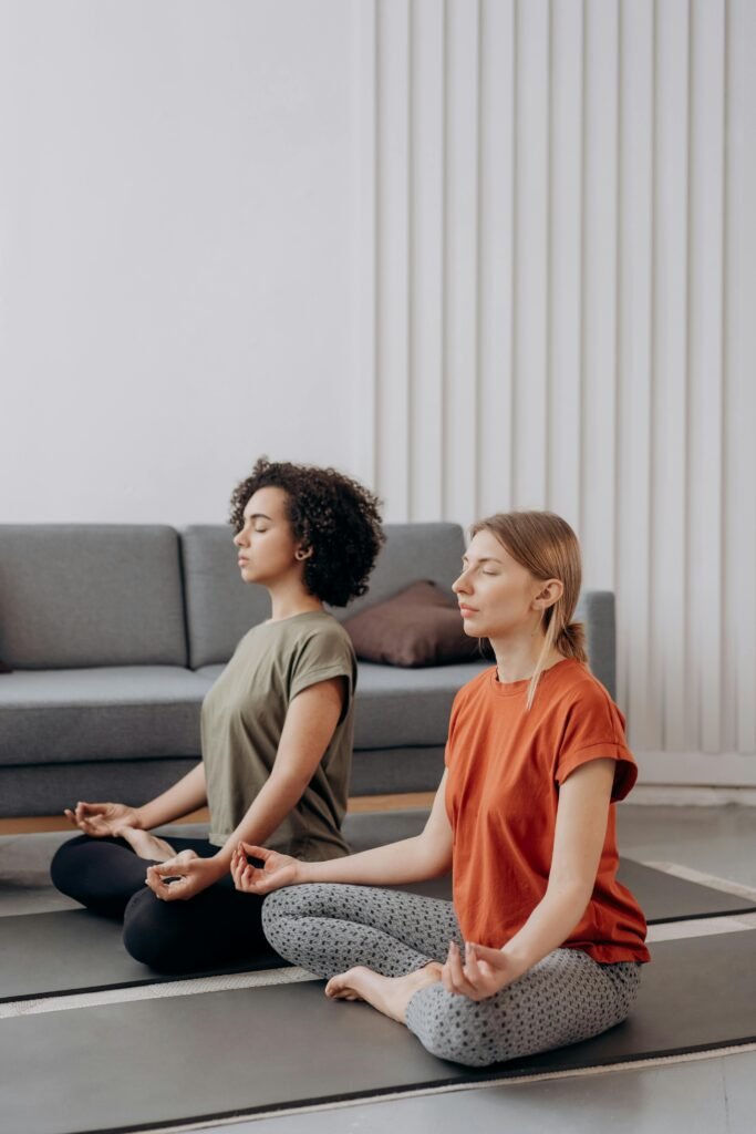 Two women meditating during a home yoga practice session for mental clarity and relaxation.