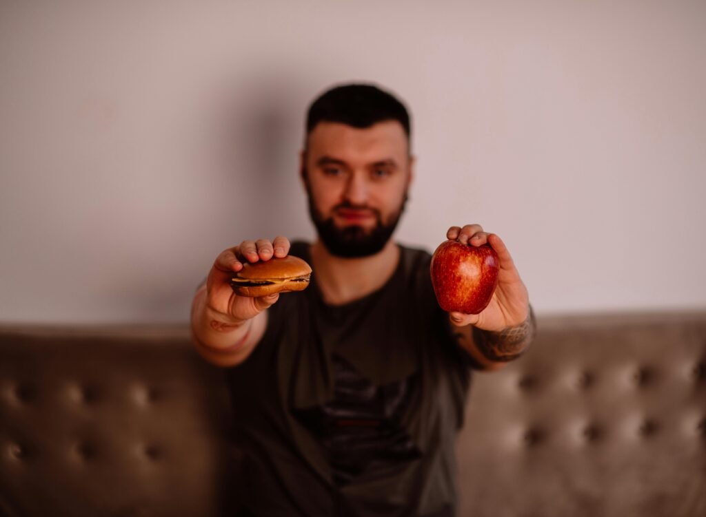 Man holding burger and apple—choosing between junk food and a healthy option