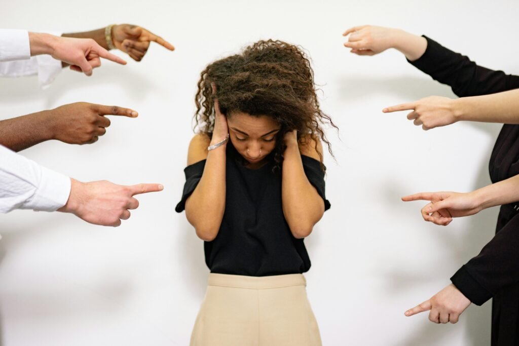 Woman experiencing social anxiety, overwhelmed and covering her ears as multiple people point fingers at her — concept of social pressure, bullying, and mental health struggles.