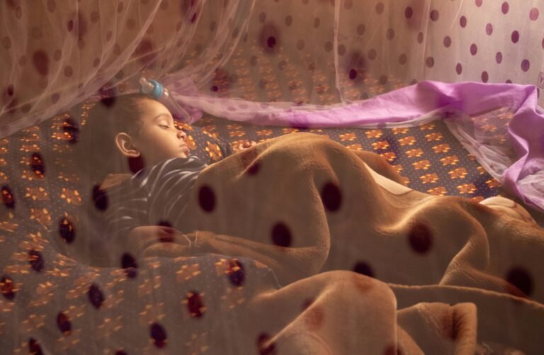 Child sleeping under a mosquito net to prevent malaria transmission in a tropical region